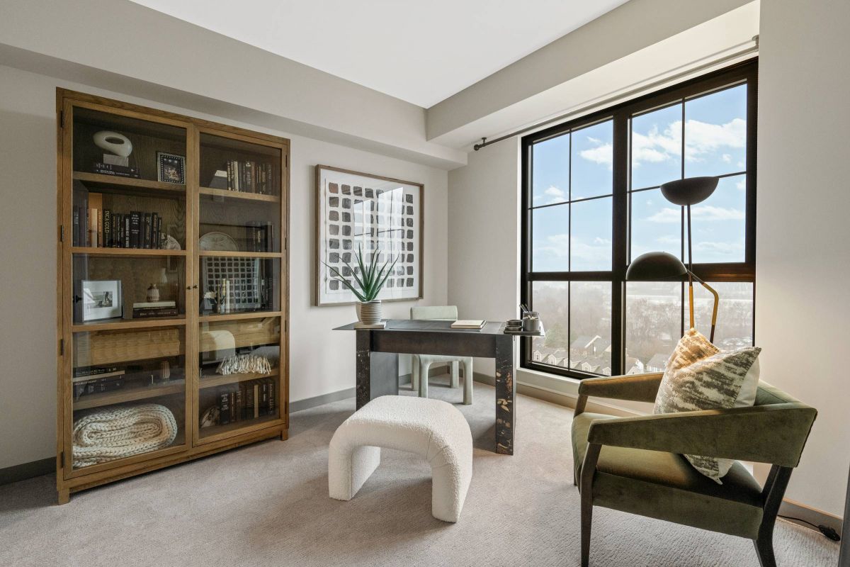 Madison West Elm apartments Modern home office with large window, bookcase, desk, green chair, and neutral decor.
